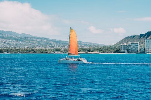 A vibrant catamaran with an orange sail sails near the coast of Honolulu, Hawaii.