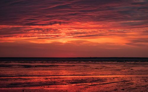 Free A stunning red sunset reflecting over a calm ocean with a dramatic sky. Stock Photo