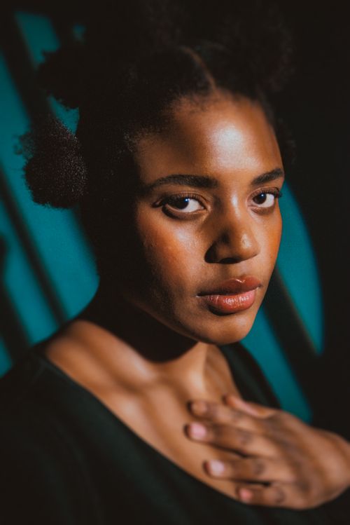 Free Stunning portrait of a young black woman with hand on chest in a Berlin studio, captured in warm, soft lighting. Stock Photo
