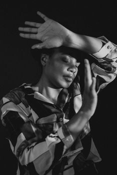 Artistic black and white studio portrait of a model with arms raised, exploring fashion through creative poses.