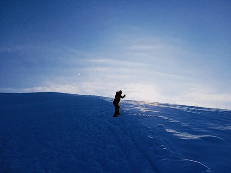 Silhouette of a skier climbing a snowy hill against a sunset backdrop, perfect winter adventure shot.