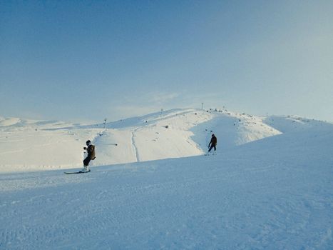 Two skiers descending a snowy slope under a clear blue sky.
