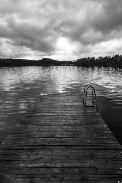 Free A tranquil black and white image of a pier extending into a calm lake under a cloudy sky in Halland, Sweden. Stock Photo