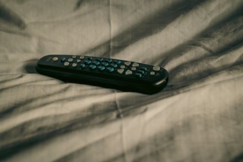 Free A remote control rests on wrinkled bed sheets, conveying a cozy and relaxed atmosphere. Stock Photo