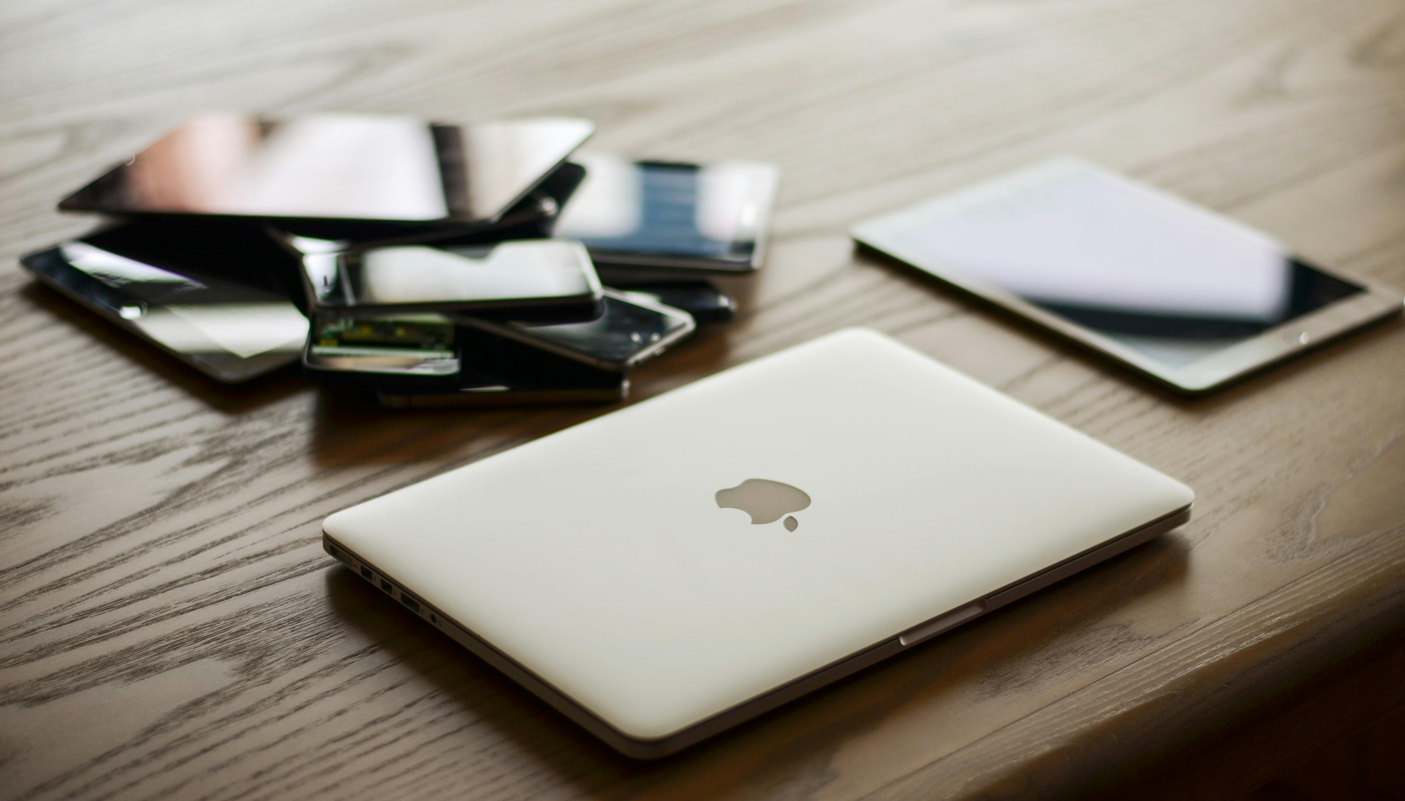 A laptop, Kindle and other devices a table.