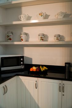 Elegant kitchen with black countertops featuring fruit and porcelain on open shelves.