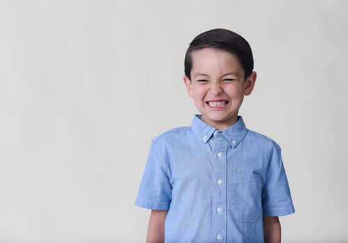 Free A cheerful child in a blue shirt making a funny face on a white studio background. Stock Photo