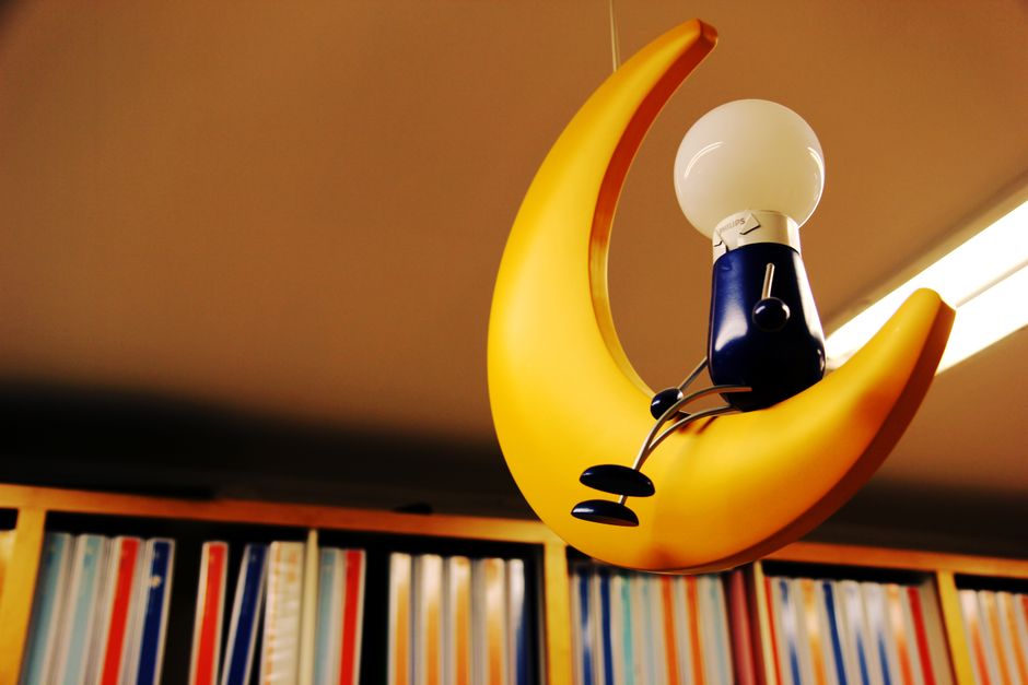 Artistic depiction of a light bulb seated on a crescent moon amidst bookshelves.