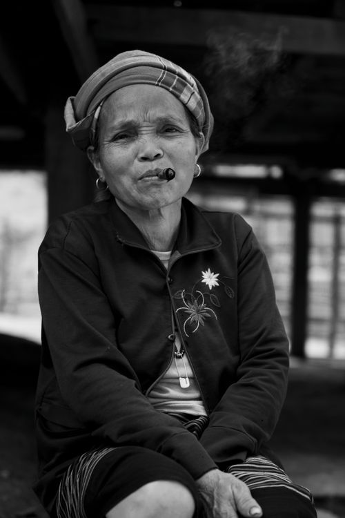 Free Black and white portrait of a woman smoking a cigar, wearing a headscarf and jacket. Stock Photo