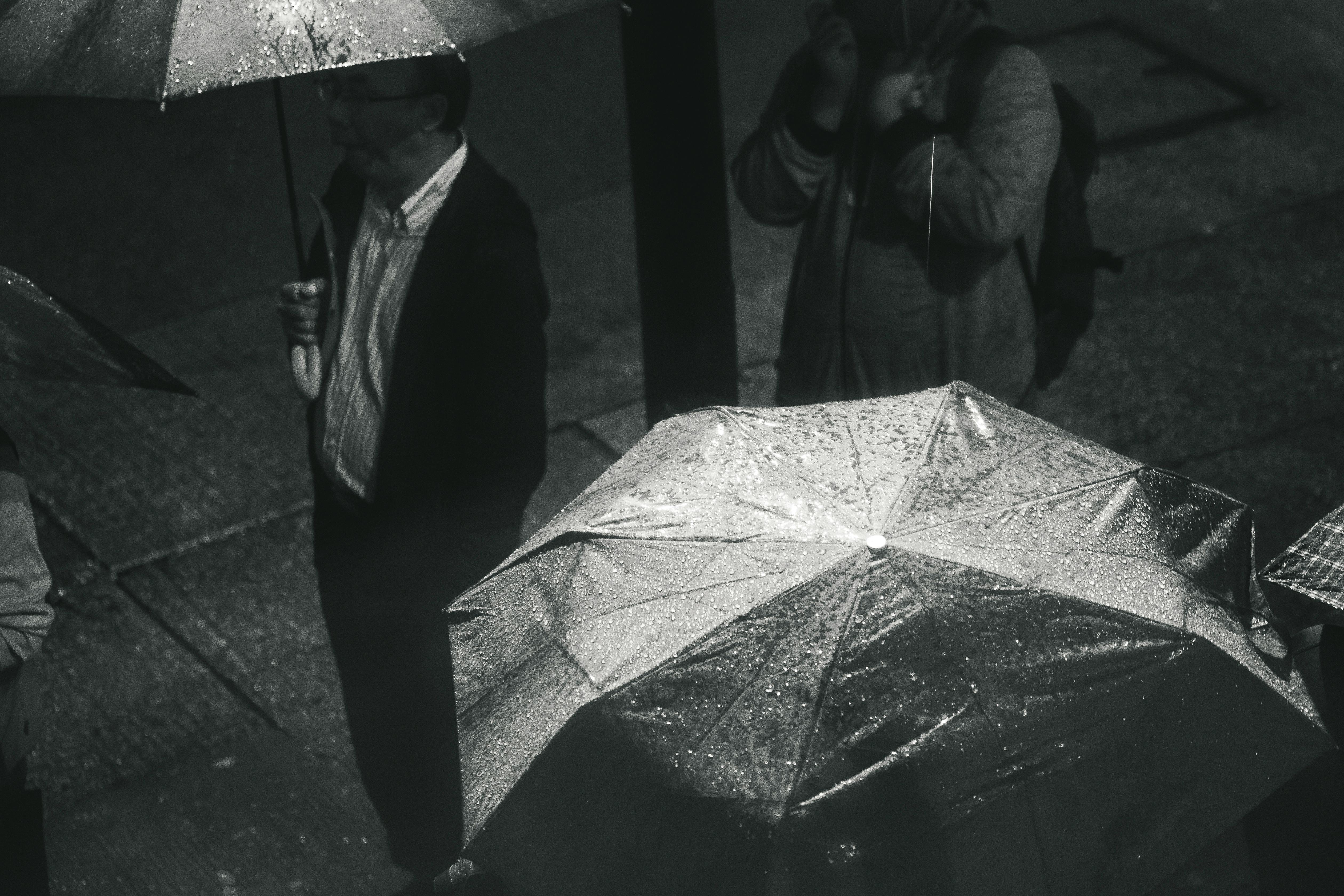greyscale photo of man holding umbrella while raining
