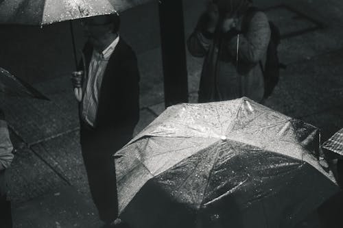 雨が降っている間傘を持っている男のグレースケール写真
