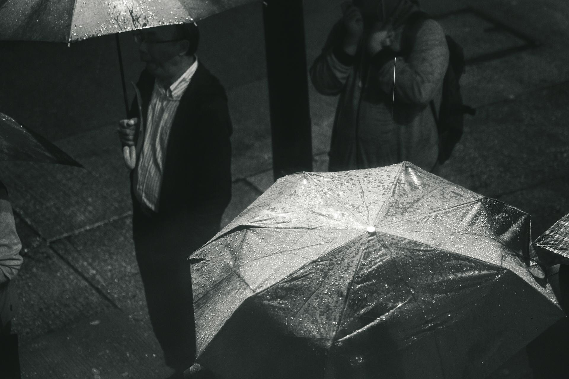 Greyscale Photo of Man Holding Umbrella While Raining