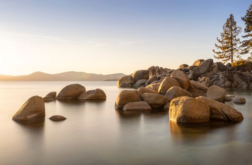 Free Golden sunset over Lake Tahoe with smooth rocks and serene water reflecting peaceful nature. Stock Photo