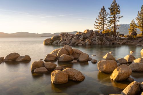 Free Breathtaking view of Lake Tahoe during sunset with rocks and trees reflecting in the calm waters. Stock Photo