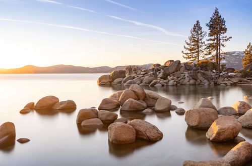 Free Tranquil scene of Lake Tahoe during sunset with rocks and pine trees along the shore. Stock Photo