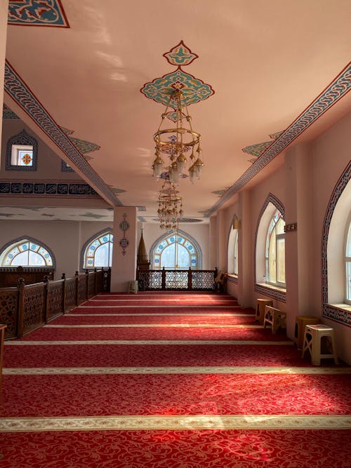 The interior of a mosque with red carpet and arched windows