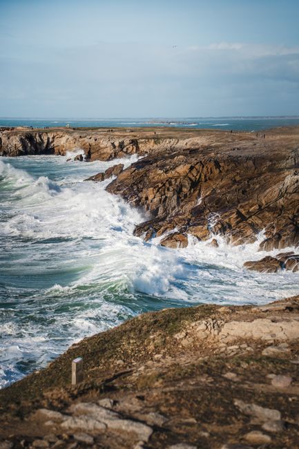 Majestic waves crash against the rocky Quiberon coastline under a clear blue sky.