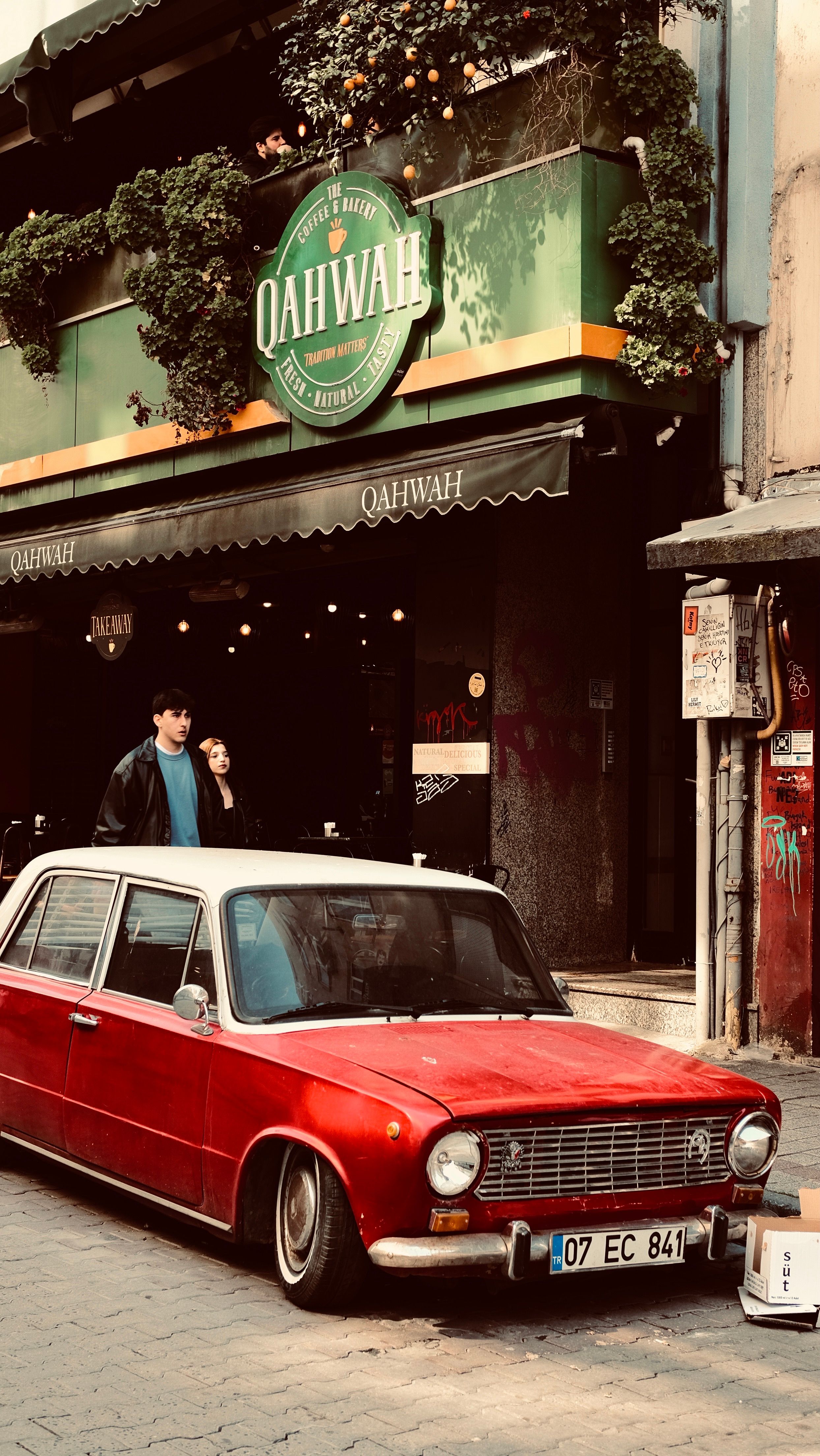 A classic red vintage car parked outside Qahwah café on an urban street in Istanbul, Turkey.