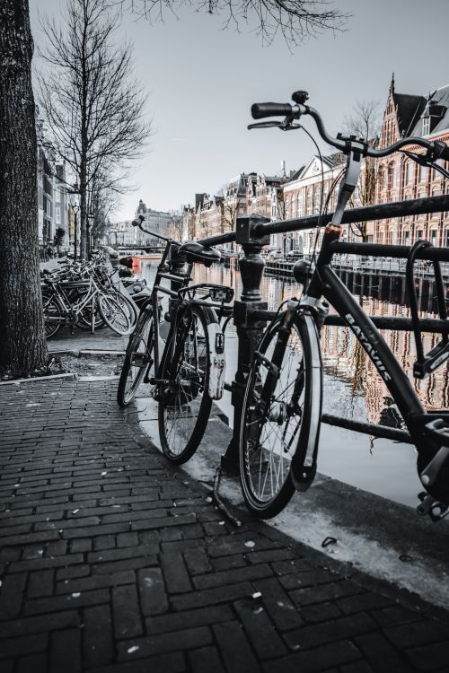 Free Scenic view of bicycles parked along an Amsterdam canal with historic buildings. Stock Photo