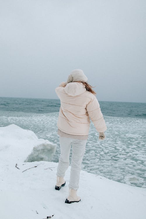 Woman in Jacket and Hat Standing on Sea Shore in Winter