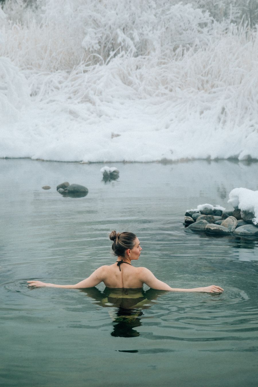 Woman shoulder-deep in a still winter lake beside a snow bank — photo by NIck Bulanov on Pexels