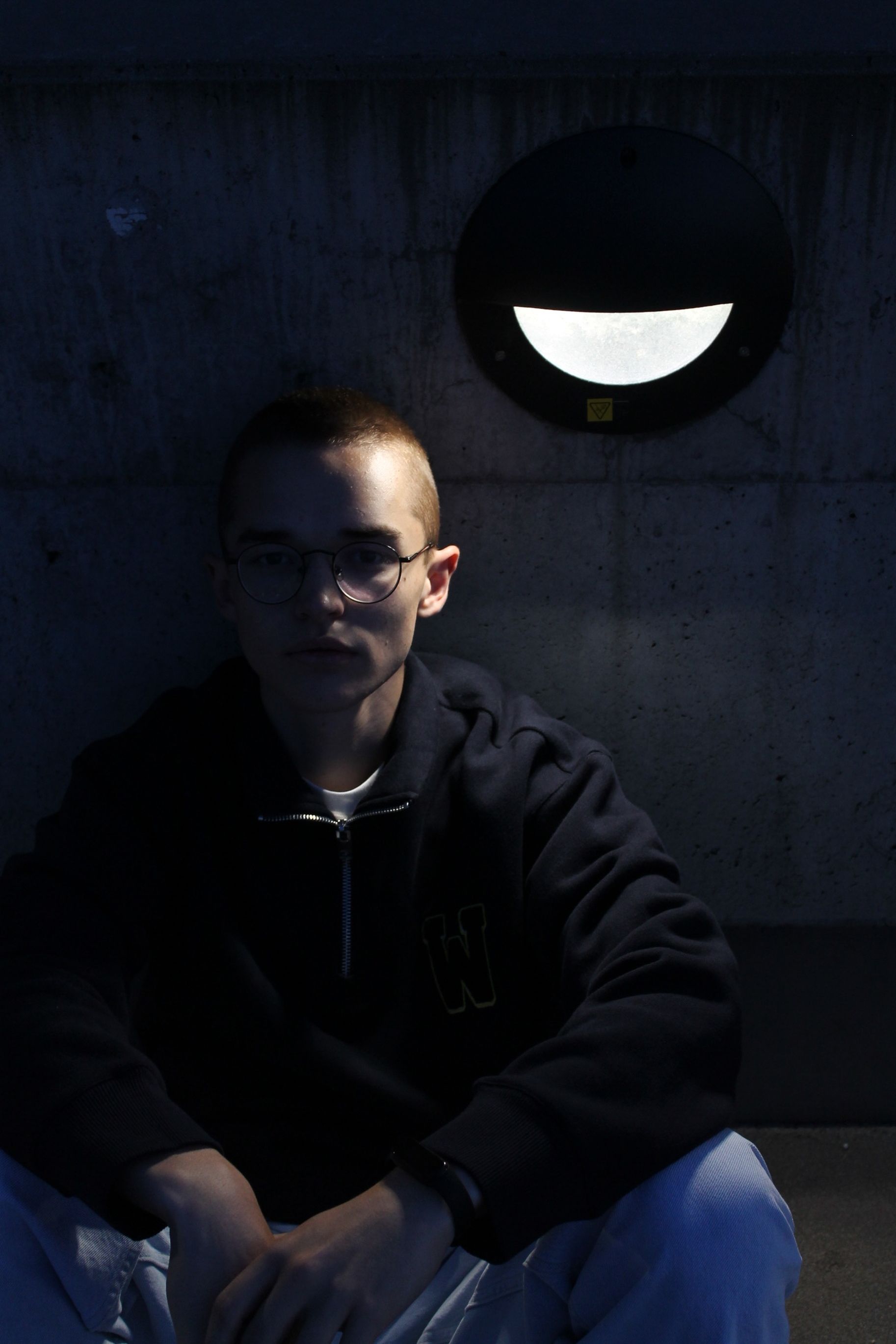 Dark and contemplative portrait of a man sitting beside wall lighting.