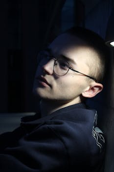 Moody portrait of a young man with glasses in dramatic lighting, evoking introspection.