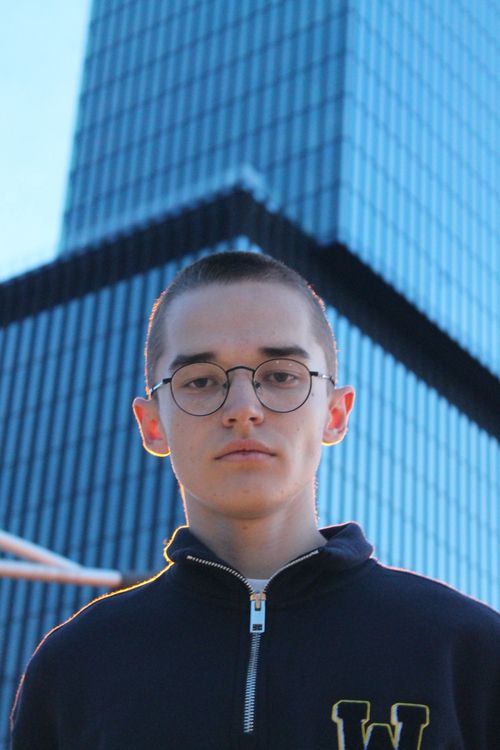 Free Portrait of a young man with glasses standing in front of a modern skyscraper during the day. Stock Photo