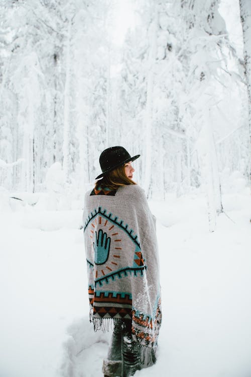 판초를 입은 여자가 겨울 숲을 걷고 있다