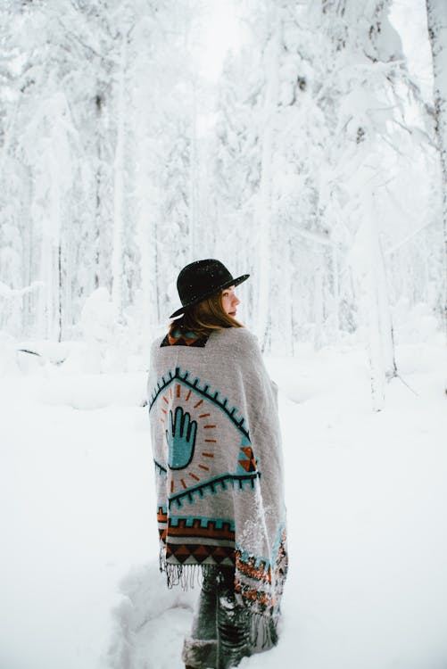 Женщина в пончо гуляет по зимнему лесу