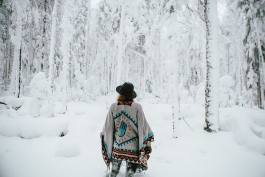 A woman in a patterned poncho wanders through a frosty forest during winter.