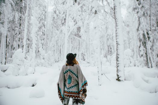 Back view of a woman in a poncho exploring a snow-covered forest during winter.
