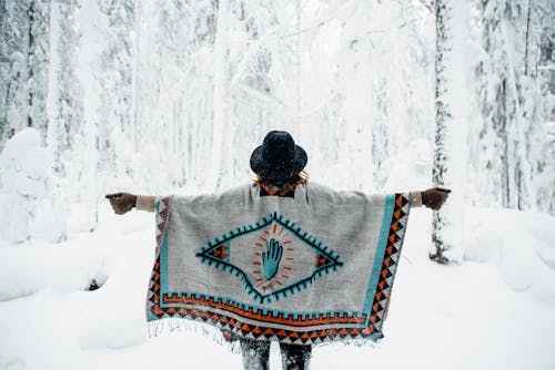 판초를 입은 여자가 겨울 숲을 걷고 있다