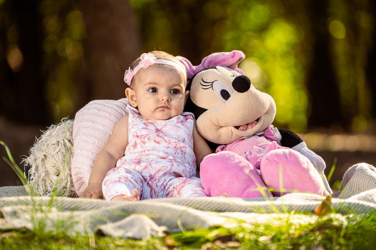 cute baby sitting on blanket with cuddly minnie mouse toy in a sunny p