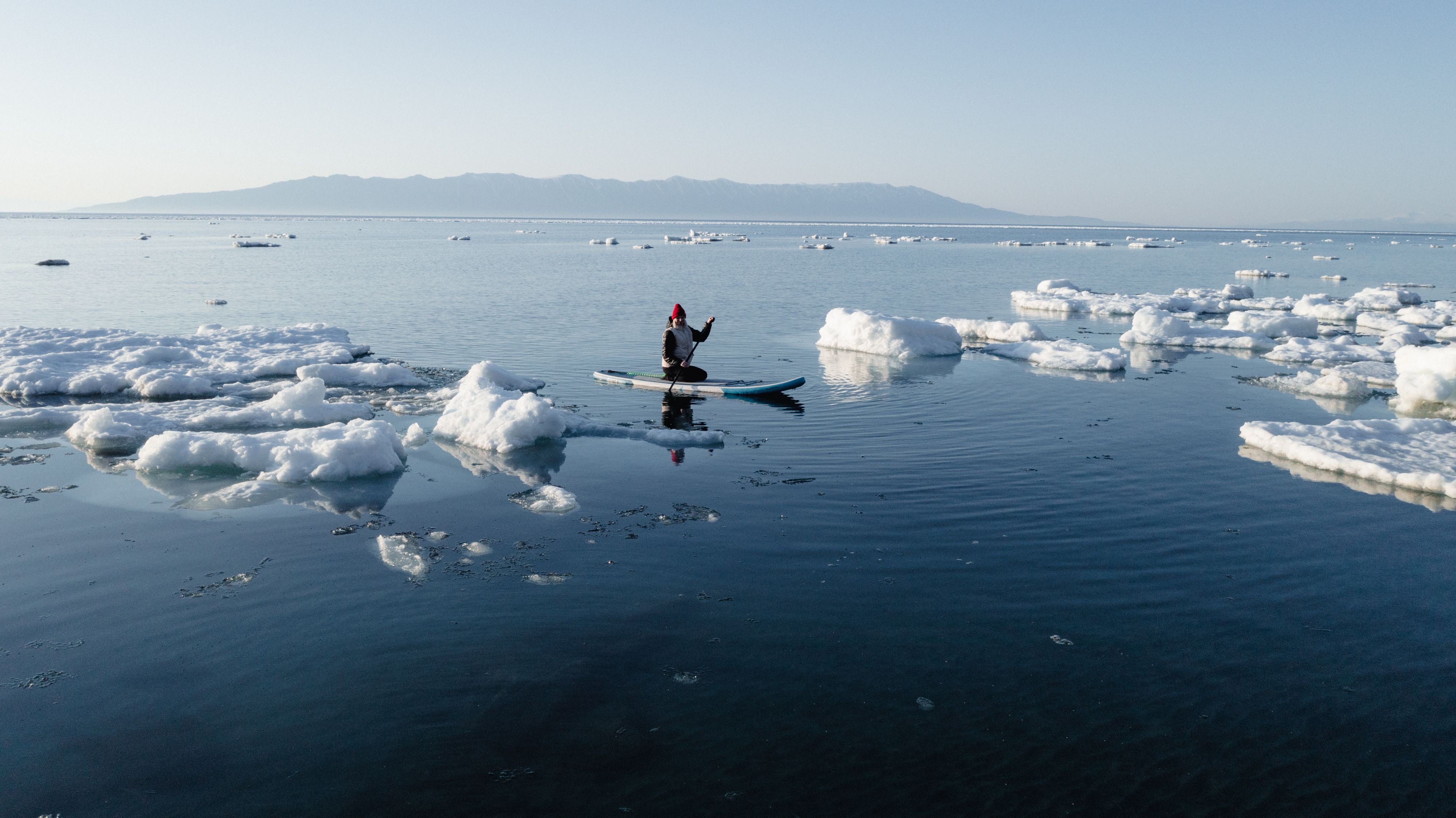Solo kayaker paddling through icy Arctic waters surrounded by ice sheets on a clear cold day