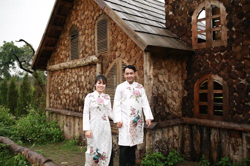 A couple in traditional clothing standing in front of a log cabin