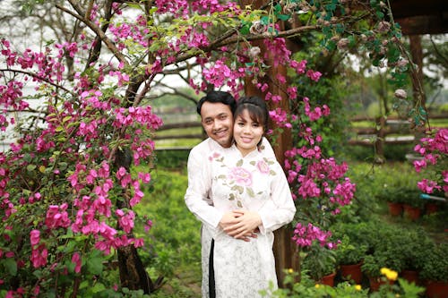 A couple in traditional dress pose for a photo in front of a flowering tree