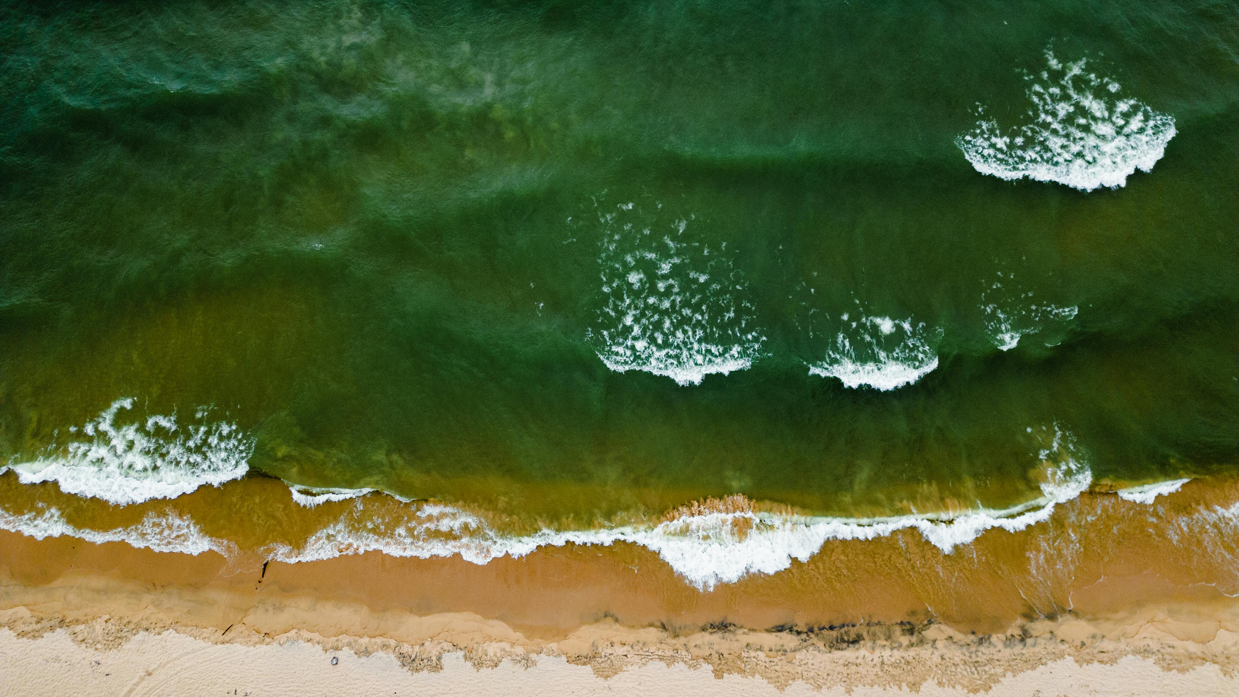 Top-down view capturing white waves rolling onto a sandy coastline.