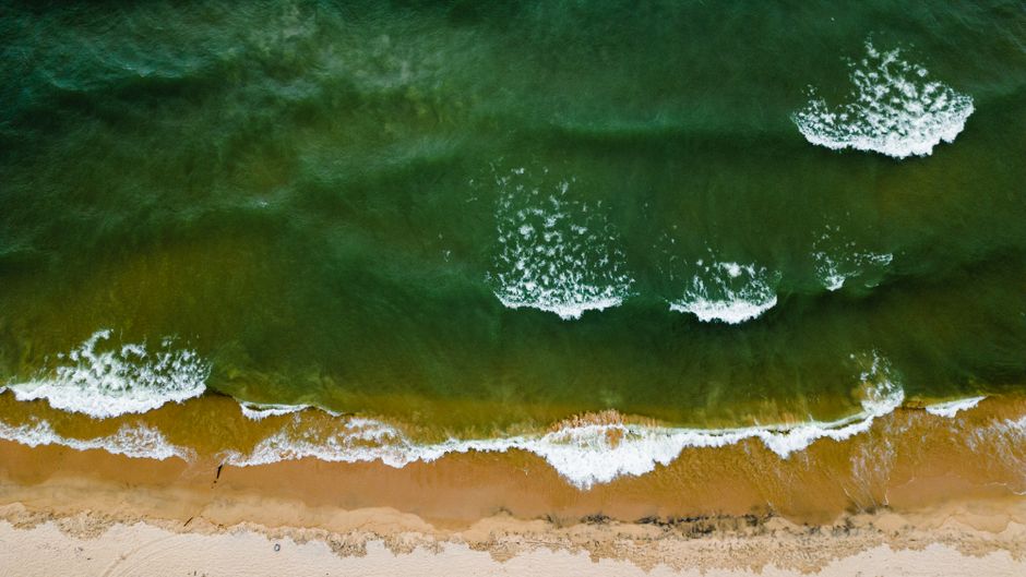 Top-down view capturing white waves rolling onto a sandy coastline.