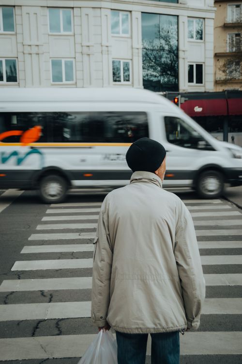 Free A senior man crossing a city street with a van passing by, depicting urban life. Stock Photo