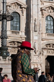 A fashionable man wearing a red hat in front of Milan Cathedral, showcasing urban elegance and cultural mix.