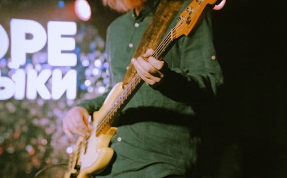 Musician playing an electric guitar during a live performance on stage with lights in background.