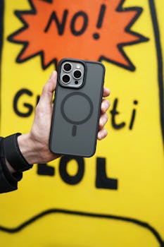 A person holding a sleek smartphone against a bold yellow graffiti backdrop.