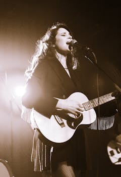 A woman passionately sings and plays guitar on stage during a live concert.