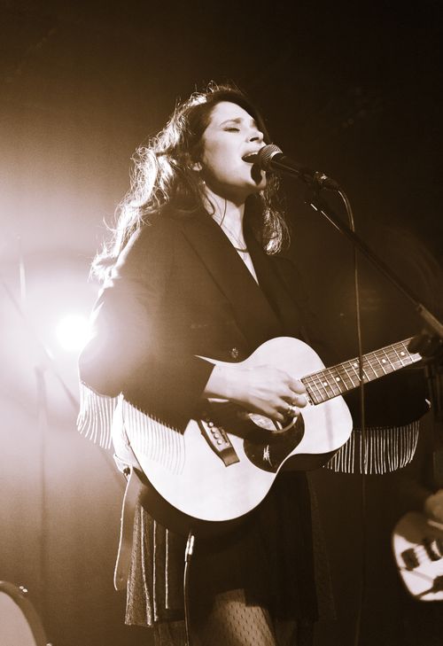 Free A woman passionately sings and plays guitar on stage during a live concert. Stock Photo