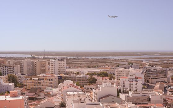Aerial view of Faro, Portugal's urban landscape with airplane flying overhead.
