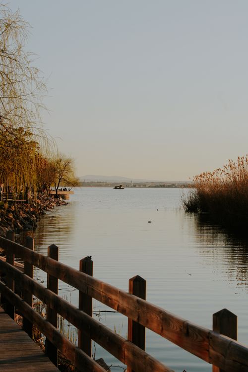 Free Serene landscape of a lakeside with a wooden fence and distant hills at sunset. Stock Photo