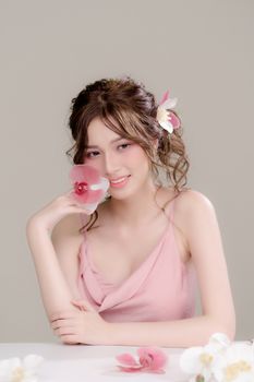 A young woman in a pink dress posing elegantly with flowers in her hair and hand.