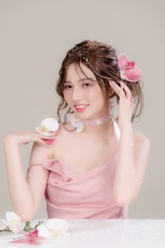 A graceful woman in soft pink attire adorned with orchids, smiling with delicate charm.