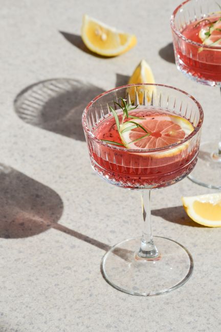 Elegant red cocktail with citrus and rosemary garnish served in a glass on a marble surface.